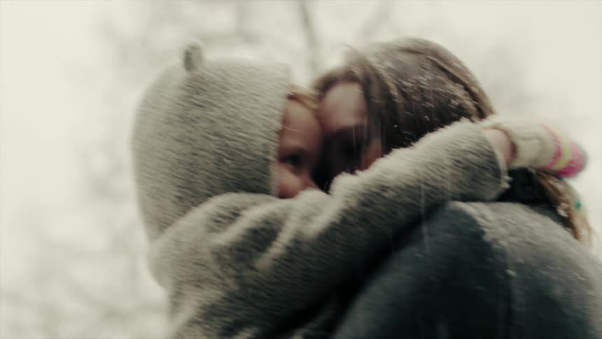 A mother is carrying and hugging her child as they stand outside while it snows