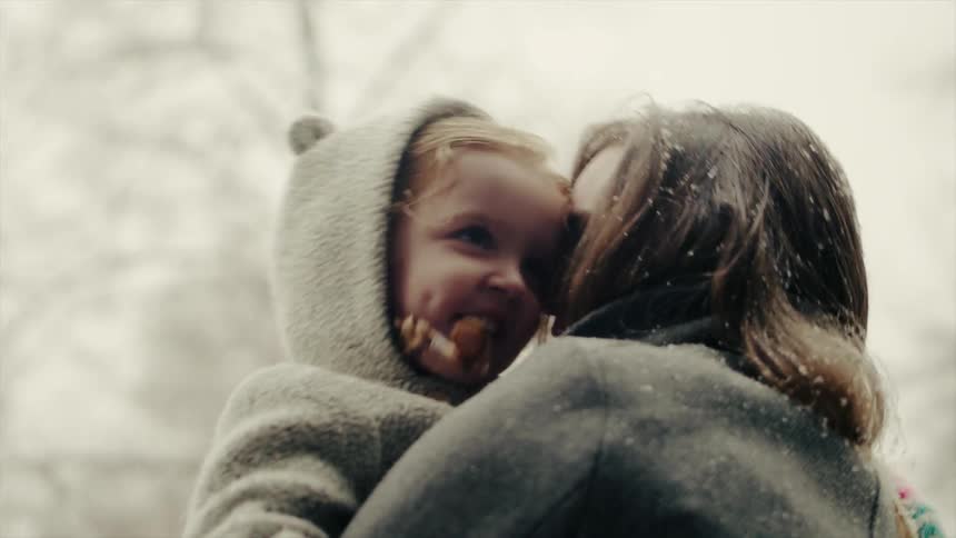 Woman carries a child outside in the yard in the snow