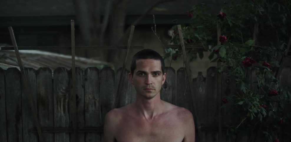 A man stands in front of a wood fence