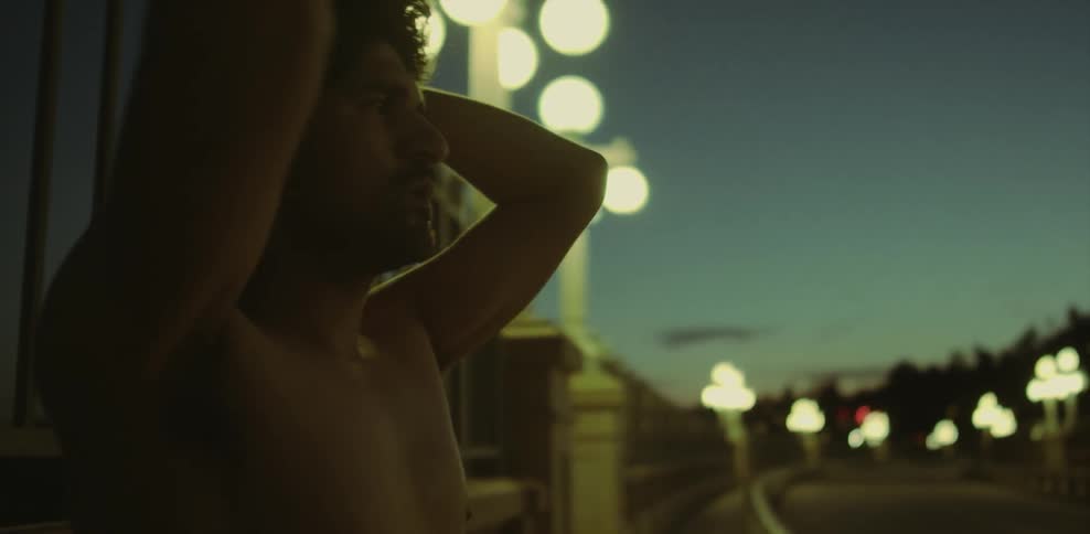 A man stretches his arms behind his head and breathes heavily outside at dusk