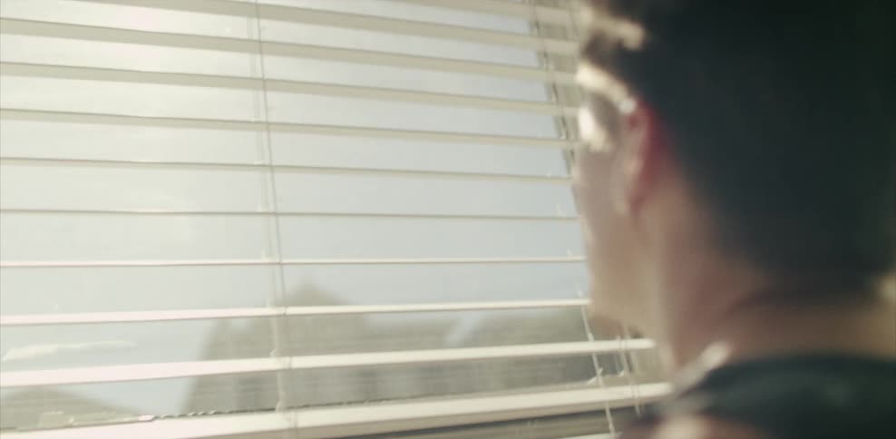Man looks through window blinds on a window on a sunny day