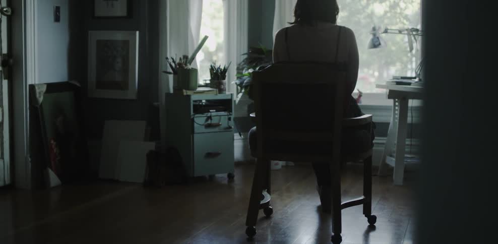 A woman sits in a chair looking out a window