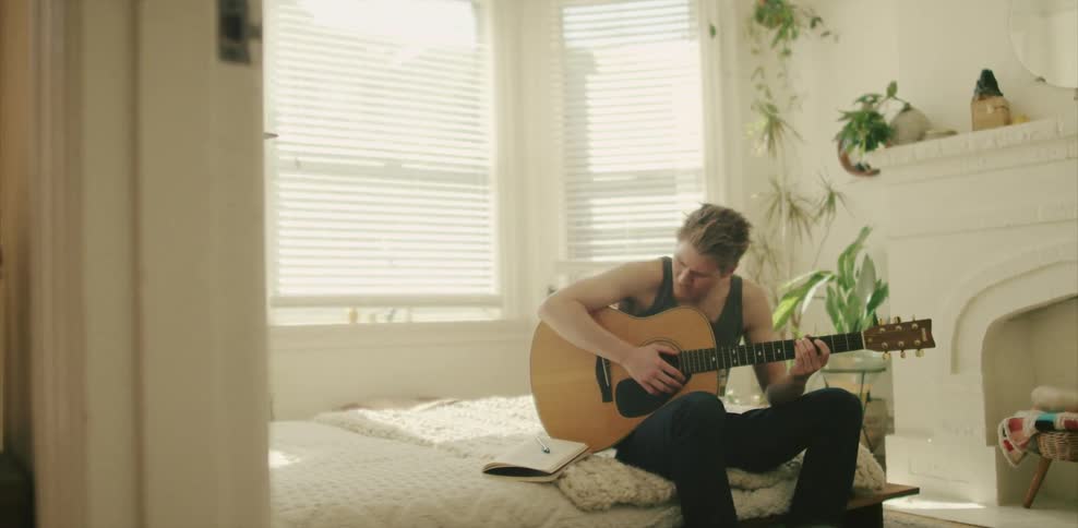 A man is sitting in bed playing the guitar