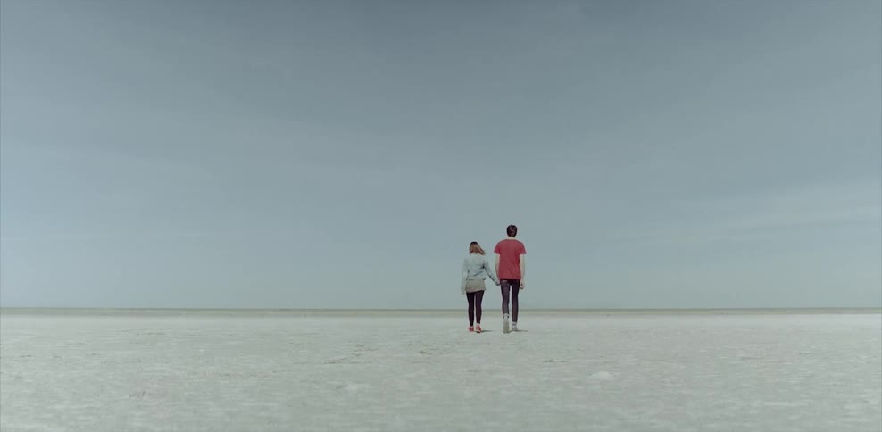 A couple walk across a flat white area on a clear day