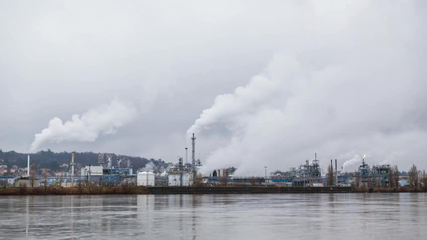 Smoke and steam rise from stacks in an industrial area on a cloudy day