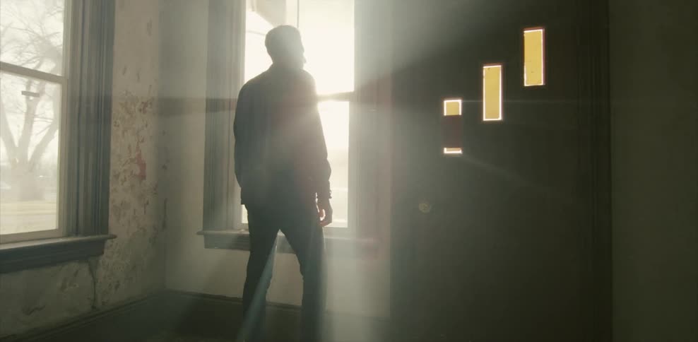 A man stands looking out the window of a vacant, rundown building