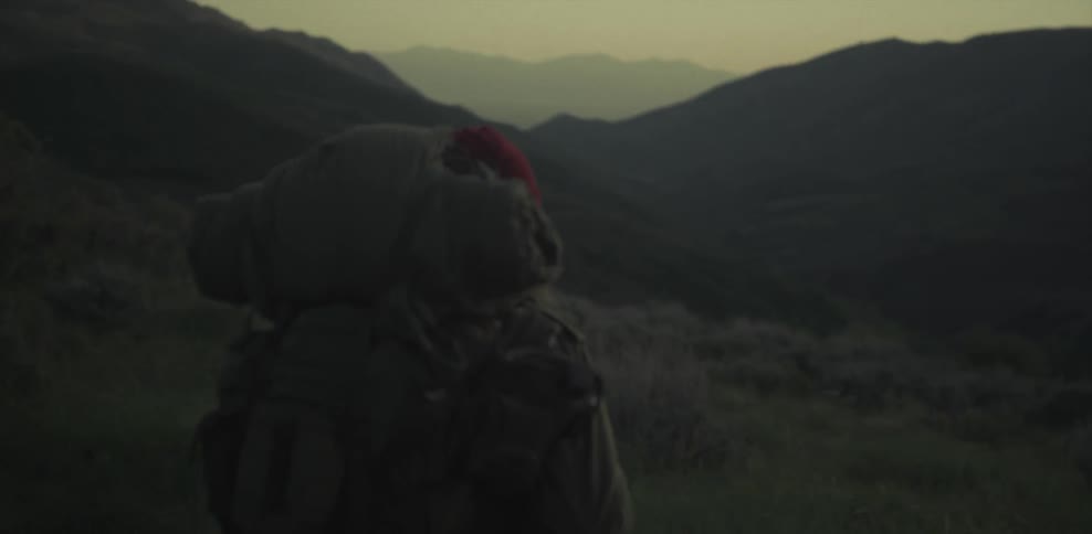 A man carrying a heavy backpack stands looking at the scenery at dusk