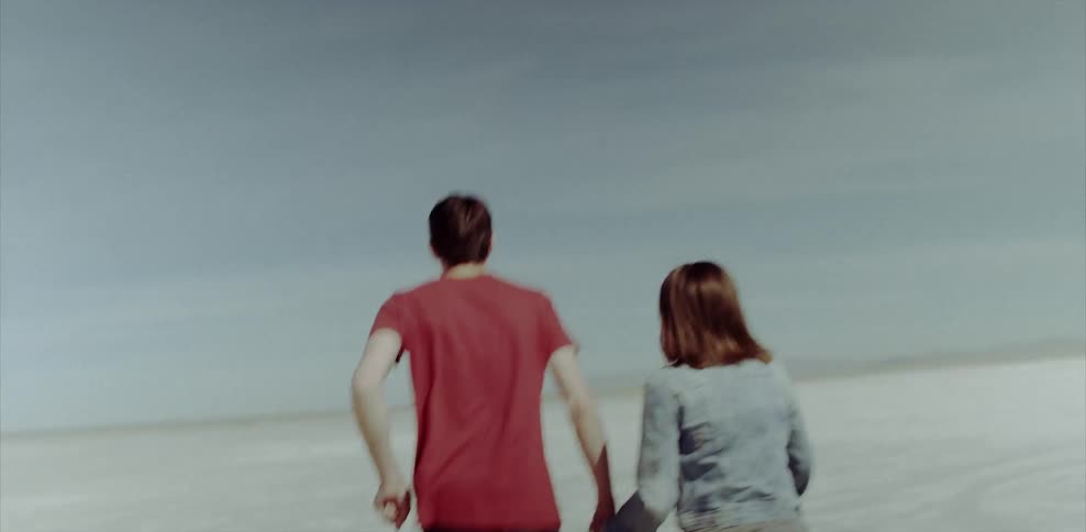 Man and woman holding hands running across flat sandy land