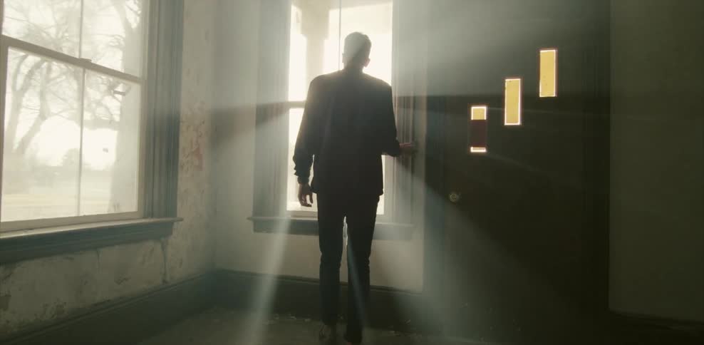 Man walking through an empty house to look out the window on a sunny day