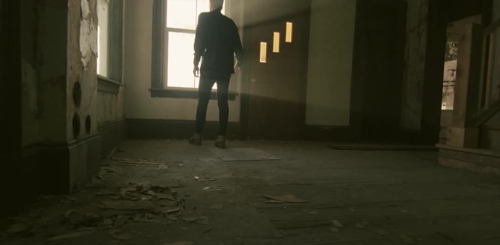 A man walks through an abandoned house and looks out the window