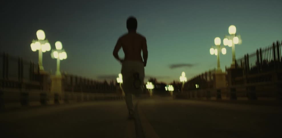 Shirtless man jogs down a bridge at night