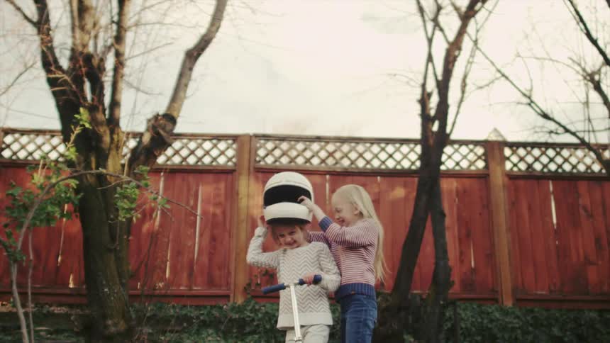 Two young girls play outside with a racing helmet