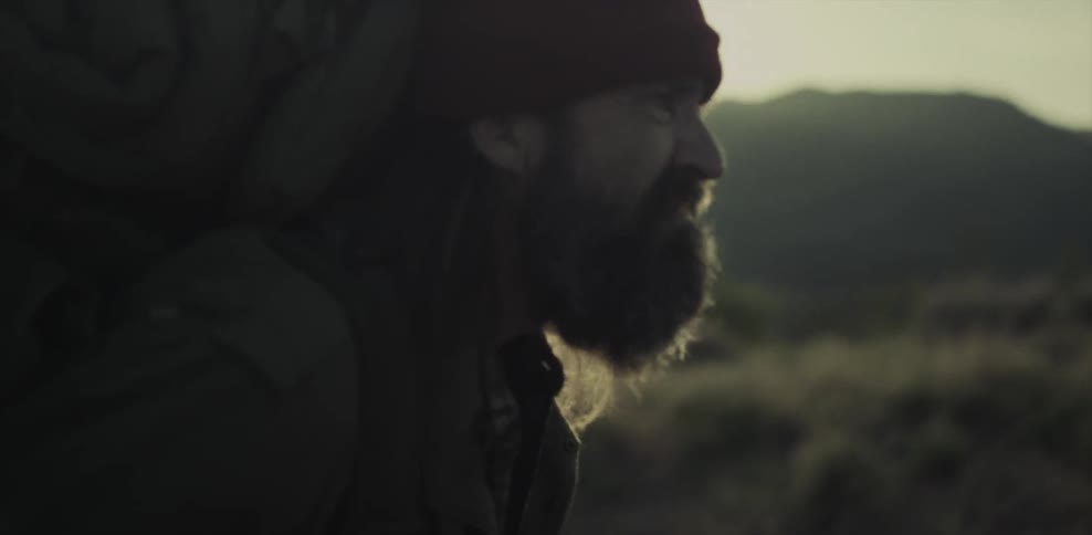 A man carrying a heavy backpack is hiking in a natural setting at dusk