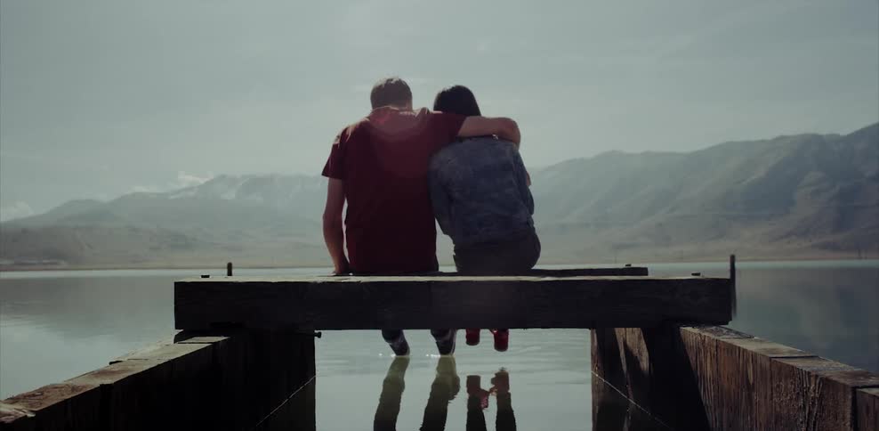 A couple sit on the end of a damaged dock