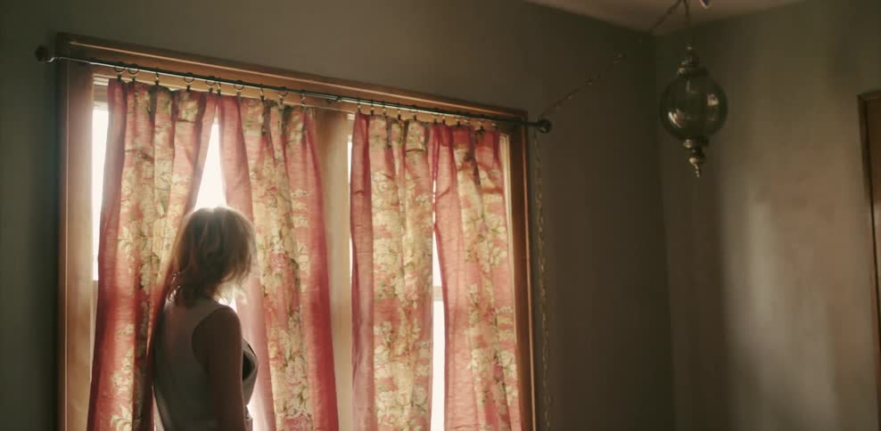 A blonde woman turns and looks out of a window