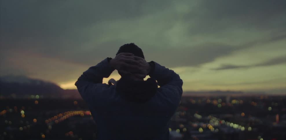A man overlooks city lights at sunset