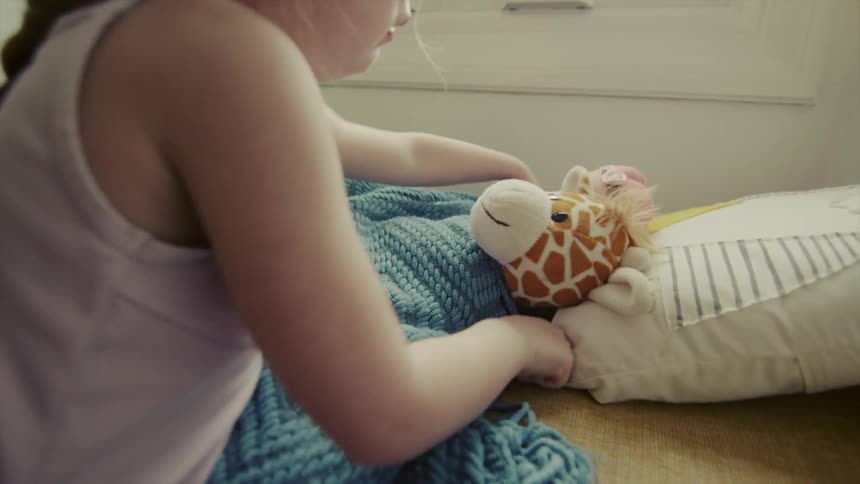 Child tucks a stuffed toy in bed