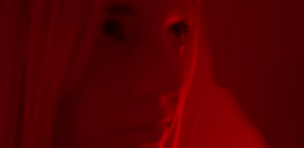 A man and woman stare at each other in a red lit room