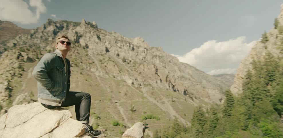 Man sits atop a rocky hill looking at mountains