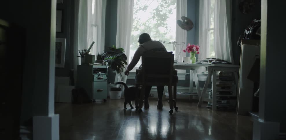 A woman pets a cat while sitting at home in front of a window