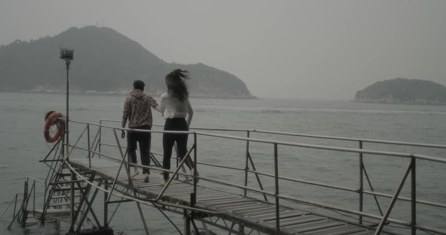 A man and woman hold hands as the run to the end of a narrow dock