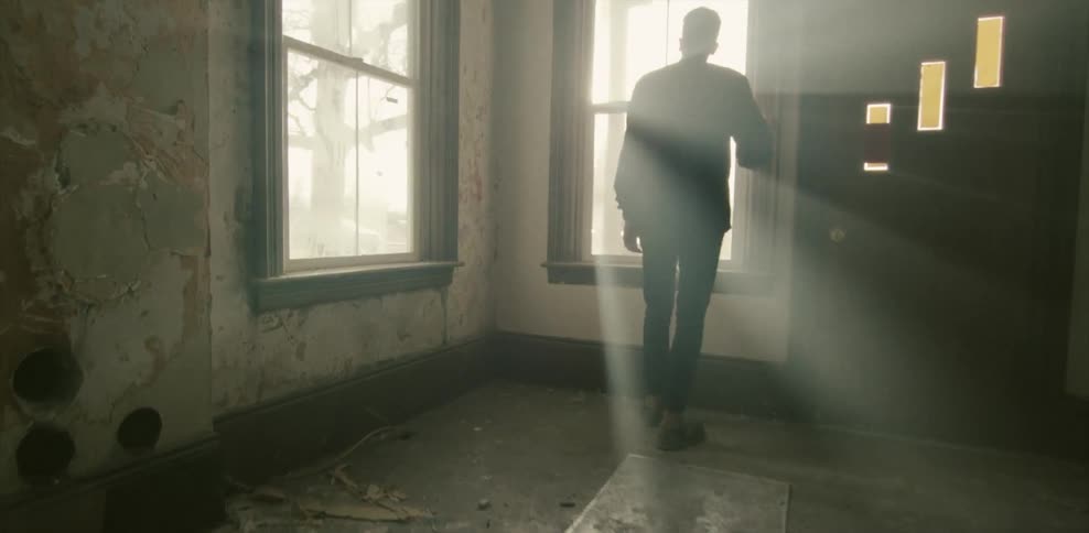 Man looking out of a window in an empty room on a sunny day