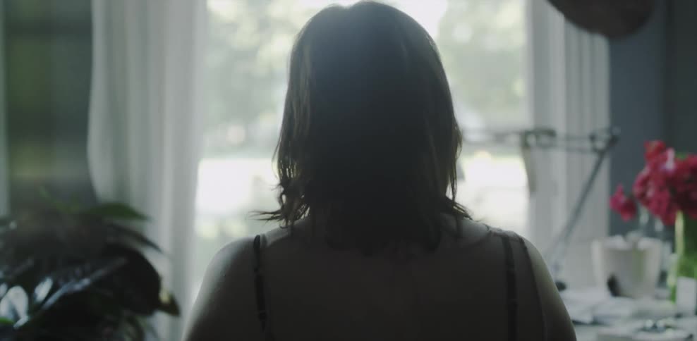 A woman walks through her dark room towards a window