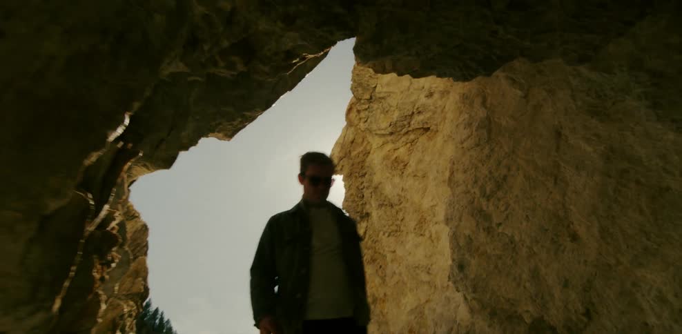 Man walking into a cave on a sunny day