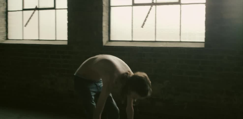 A thin and shirtless man lifts a barbell over his head