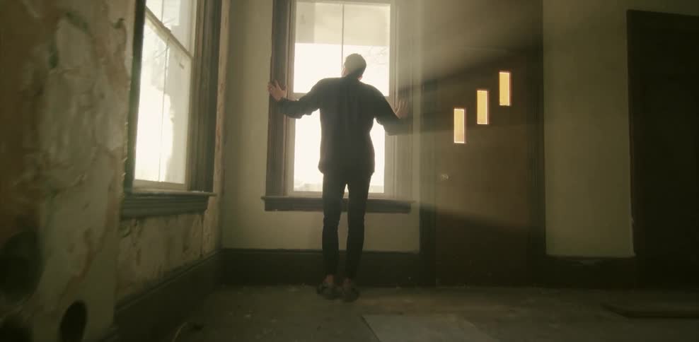 A man in an abandoned house looks out of a window