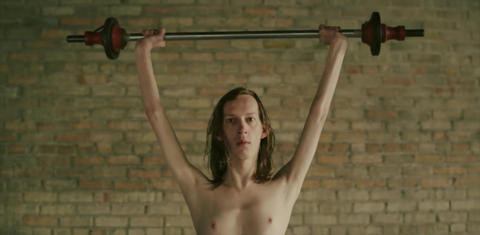 A skinny man lifts up a barbell above his head