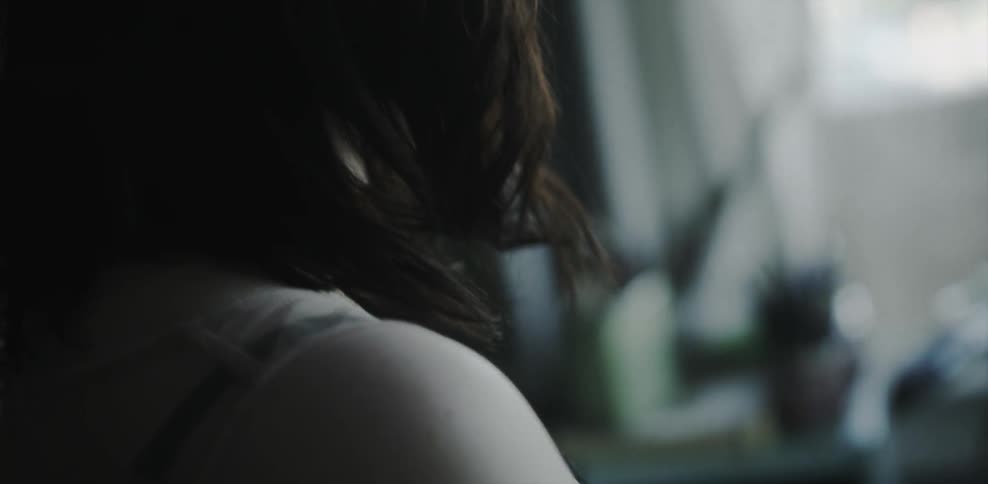 A woman stands in a dark room looking out a window