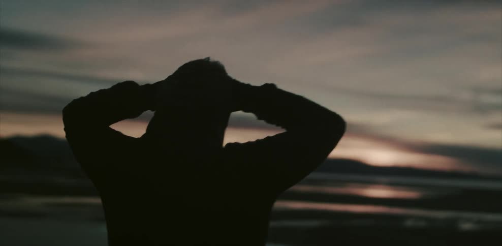 A man stands outdoors while the sun sets over the mountains