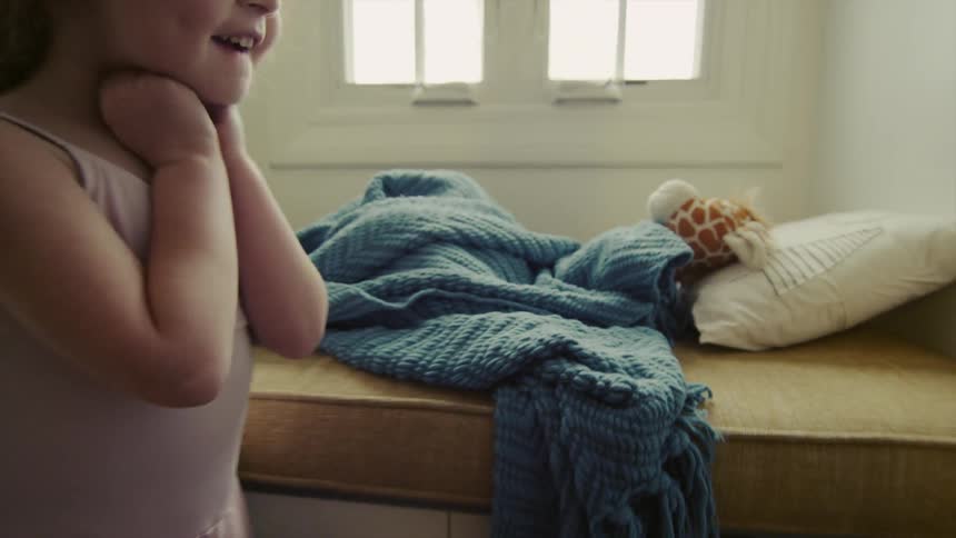 A little girl rests a stuffed giraffe on a pillow and under a blanket