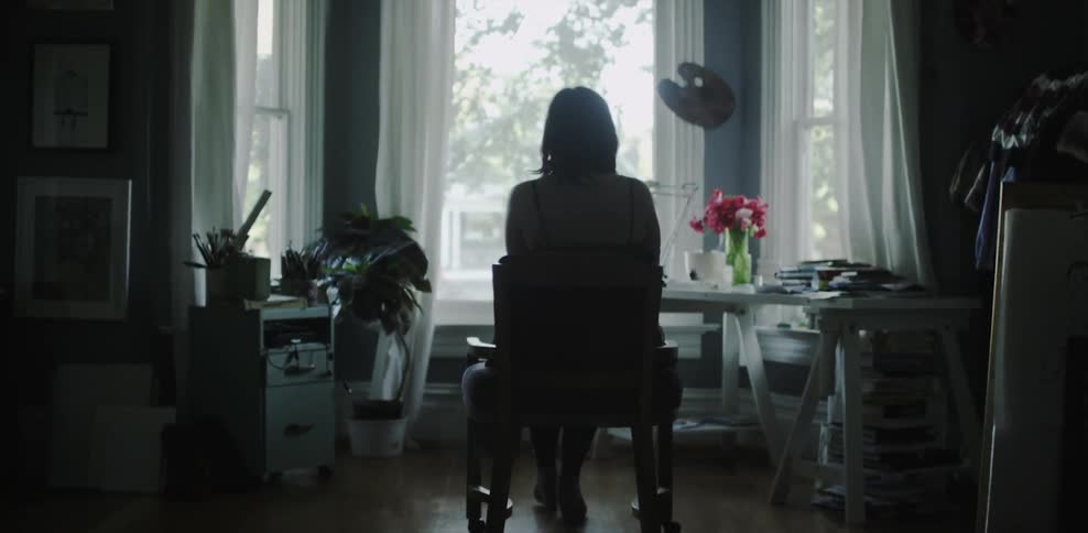 A woman sitting on a chair in the middle of a room looking out the window