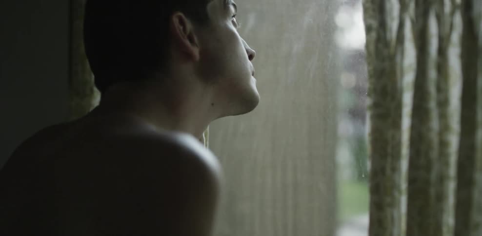 Shirtless man stands looking out a window