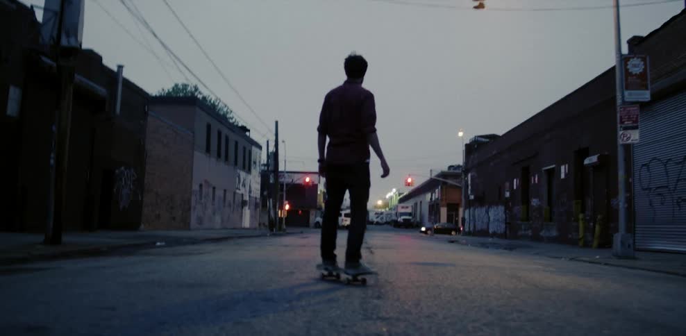 A man skateboards on a city street at dusk