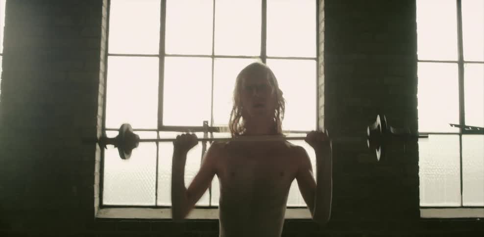 A skinny man lifts up a barbell above his head