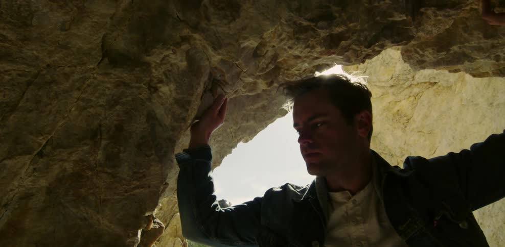 A man looking inside a cave with the sun in the back