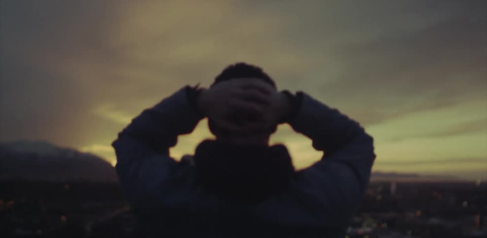 A man rubs his head while he watches a city