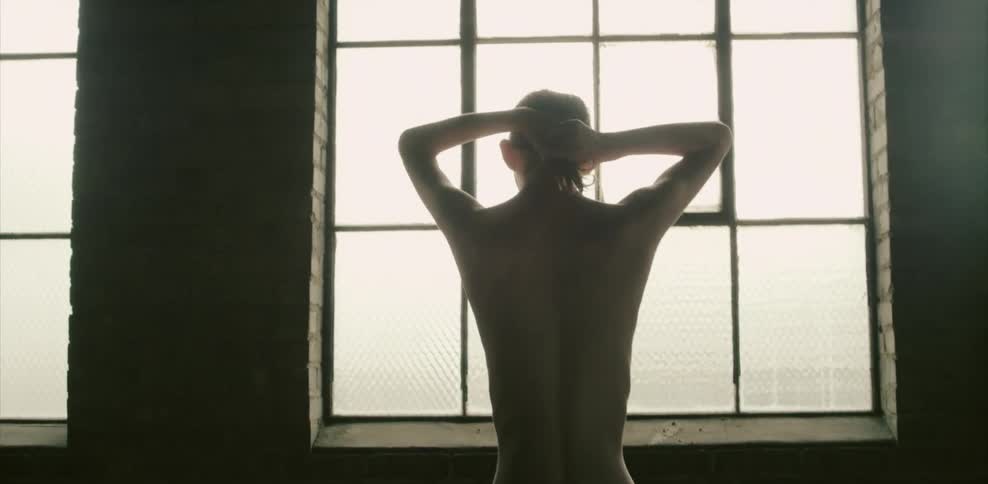 A man pulls his hair together stares out a slatted window