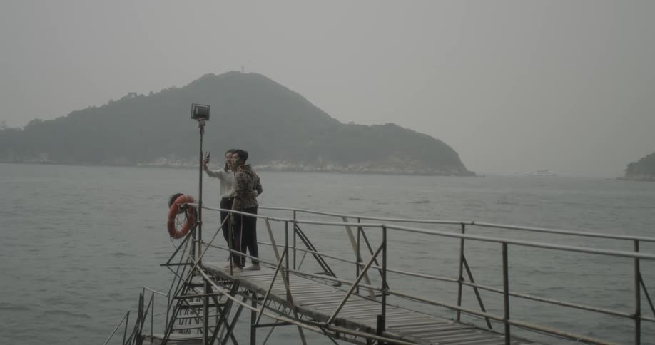 A man and woman take a selfie on an ocean pier