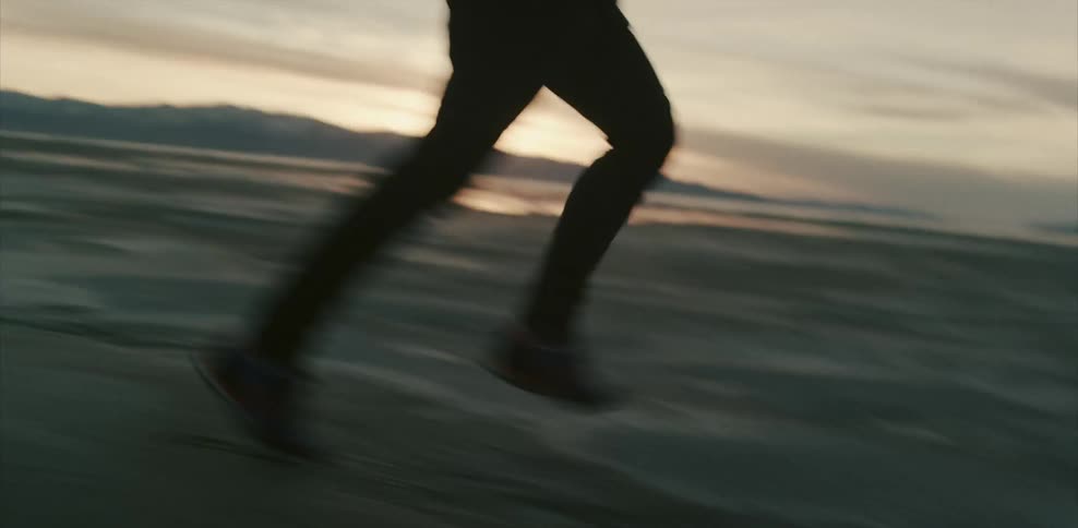 Man running across a sandy landscape at sunset