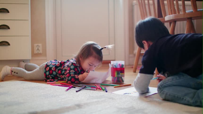 Two children color on paper on the dining room floor