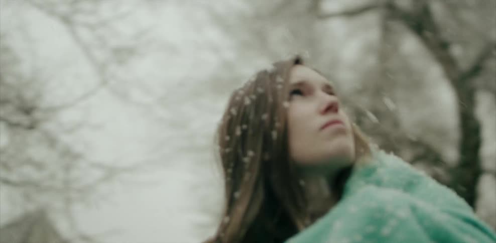 Woman outdoors watching the snowfall as she is covered with a green blanket