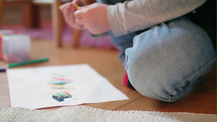 A young boy colors while sitting on the floor