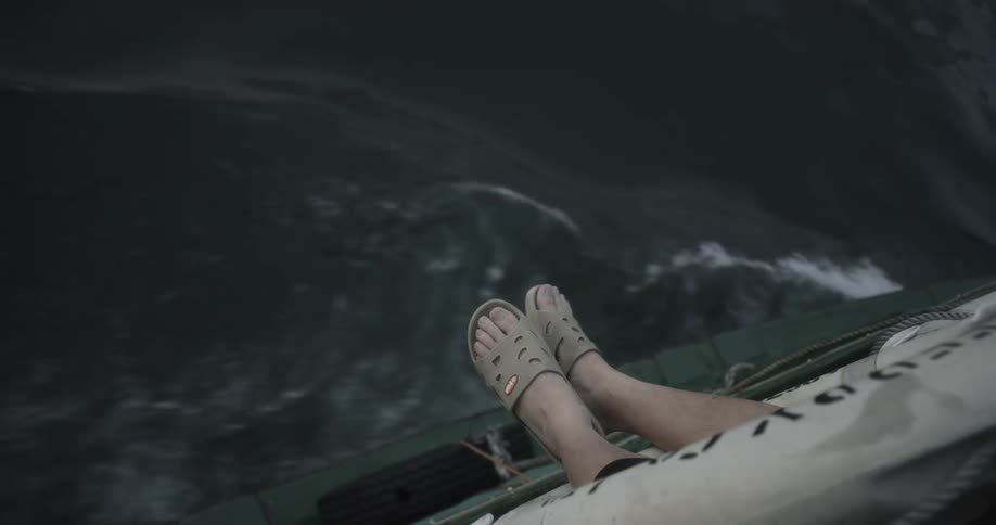 A person's feet hang over the side of a moving boat