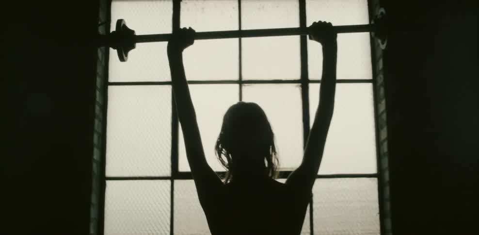 A tall skinny man holds up a barbell above his head