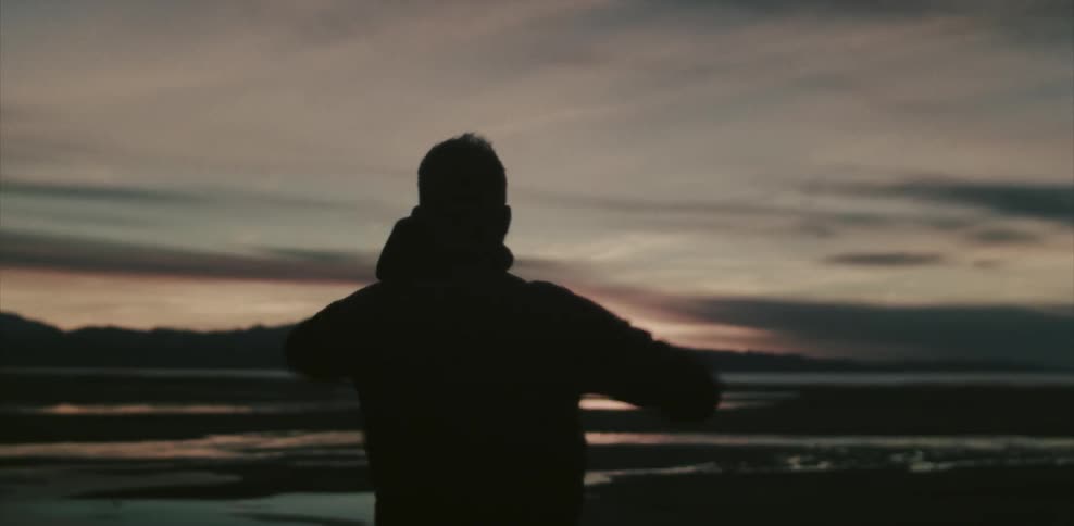 Man stretching outdoors at sunrise while wearing a hoodie
