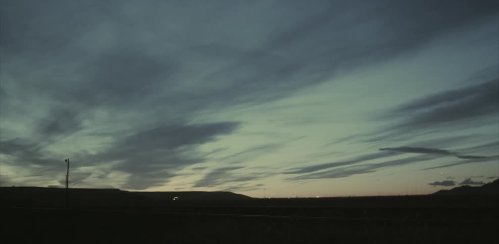 Wispy clouds hover over a desert road at dusk